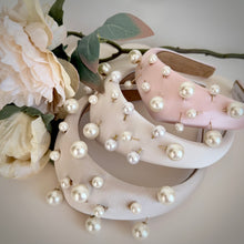 Load image into Gallery viewer, Three padded satin headbands in ivory, white and blush pink, each embellished with scattered faux pearls in varying sizes, are styled together with soft ivory blooms and eucalyptus foliage. The elegant composition highlights the luxurious textures and contemporary, feminine design against a clean neutral background.
